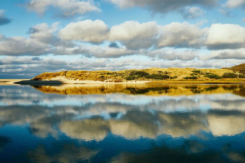 Dunes and clouds reflected in still river water, Margaret River mouth